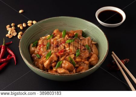 Kung Bao Chicken On A Black Background. A Chinese Dish With Chicken, Chili, Peanuts, Sauces And Onio