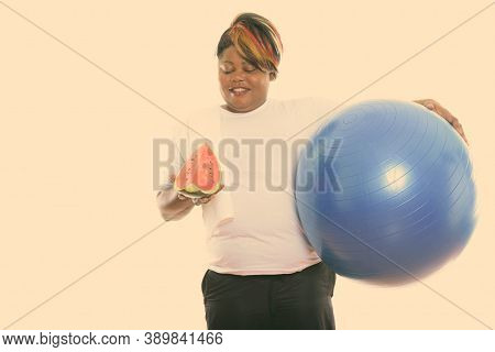 Studio Shot Of Happy Fat Black African Woman Smiling While Holding Exercise Ball And Looking At Slic