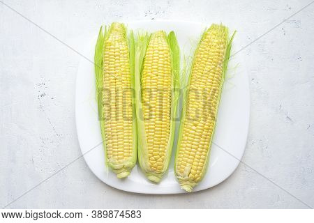 Fresh Corn Ears With Green Leaves On A White Square Plate On A Light Vintage Background. Top View