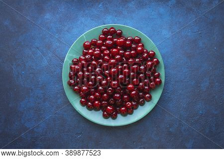 Round Green Plate With Fresh Red Delicious Cherries On Blue Background. Top View