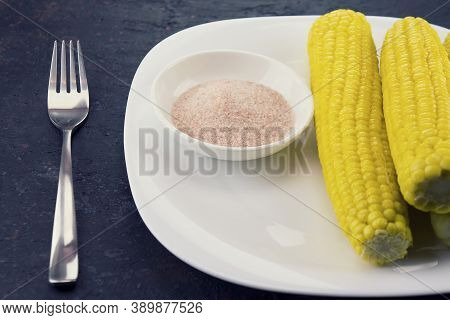 Organic Cooked Corn With Pink Himalayan Salt On A White Plate And Fork. Dark Blue Background. Close-
