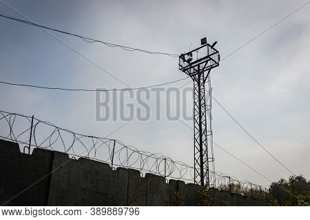 An Iron Tower Behind An Impregnable Fence. Wires Stretch To The Tower. Fence With Barbed Wire. A Tow