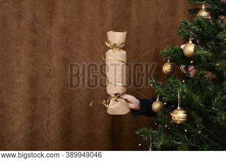 Extended Childrens Hand With A New Years Flap Surprise. From Behind A Loaded Christmas Tree.