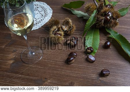 Chestnuts And A Glass Of White Wine On A Wooden Table In Autumn