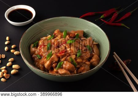 Kung Bao Chicken On A Black Background. A Chinese Dish With Chicken, Chili, Peanuts, Sauces And Onio