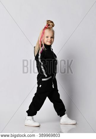 Smiling Blonde Kid Baby Girl With Girlish Hairstyle And Colorful Braids Wearing Warm Black Jumpsuit 