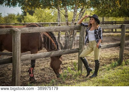 American Woman On A Horse Farm. Portrait Of Girl In Cowboy Hat With A Horses. Hippotherapy At Nature