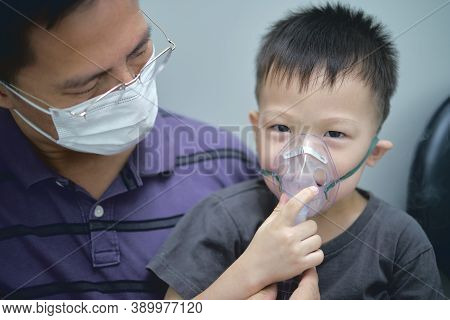 Asian Father Helping His Toddler Son With Inhalation Therapy By The Mask Of Inhaler. Sick Smiling Li