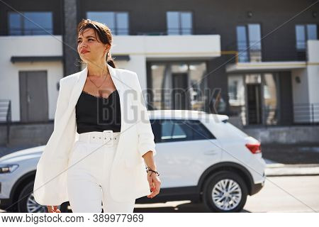 Confident Woman In White Formal Wear Outdoots Near Her White Car.