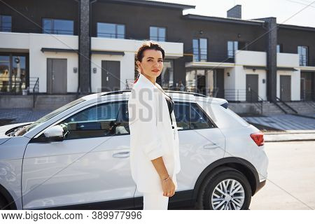 Confident Woman In White Formal Wear Outdoots Near Her White Car.