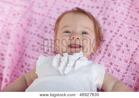Sweet Little Baby Girl Lying On Her Back Wearing A White Jacket, Looking At The Camera And Laughing