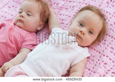 Sweet Little  Twins Lying On A Pink Blanket. They In Pink And White Dresses.