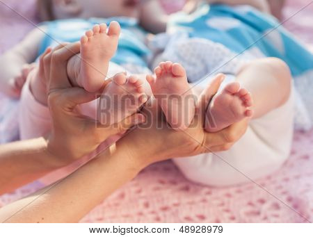 Legs Newborns In Parents Hand. Twins Lying On A Pink Blanket.