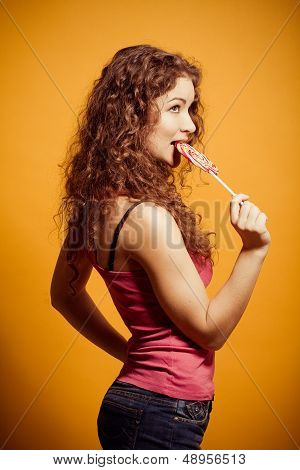 happy young woman eating lollipop on yellow background