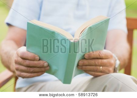 Close-up mid section of a relaxed senior man reading a book at the park