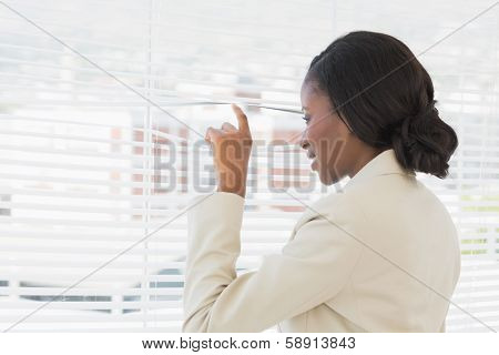 Rear view of a young businesswoman peeking through blinds in office