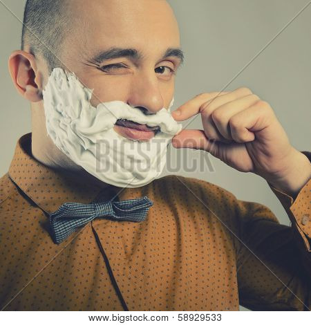 Hipster. Funny portrait of trendy man making moustache and beard of shaving foam and gives wink, toned.