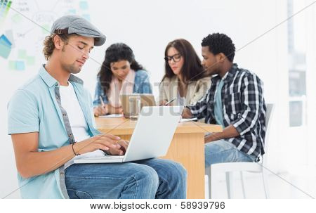 Concentrated casual man using laptop with group of colleagues behind in a bright office
