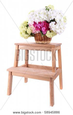 Wicker basket with flowers on small wooden ladder, isolated on white
