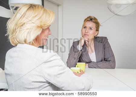 Two woman talking about the latest gossip on their coffeebreak in the office attentively listening to eachother