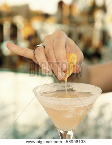 Female bartender is squeezing orange juice into a cocktail glass, toned, vignetting added
