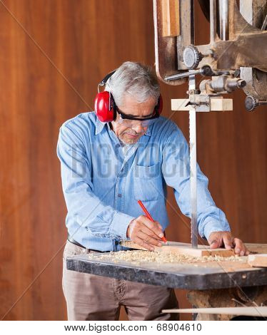 Senior carpenter marking on wood while cutting wood with bandsaw in workshop