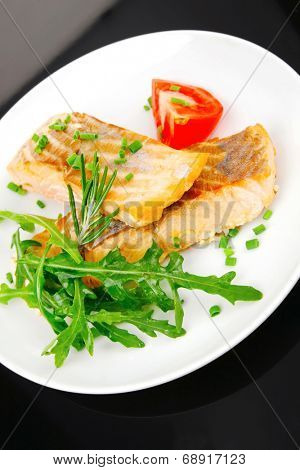 healthy fish cuisine  : baked pink salmon steaks garnished with tomatoes and rocula on white dish isolated over black background