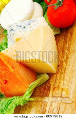 fresh aged french cheeses chops on big cutting board with tomatoes olive oil, rye breadm and green chives isolated over white background