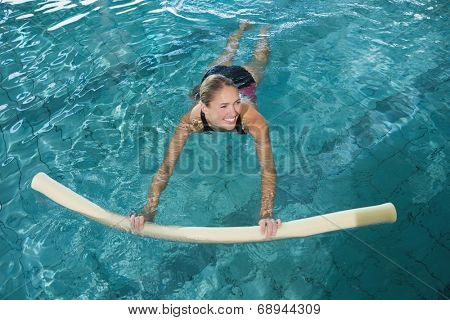 Fit blonde swimming with foam roller in swimming pool at the leisure centre