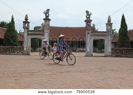 Vietnamese women cycling in front of a temple