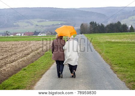 Women In Rain Under An Umbrella In Rural Landscape