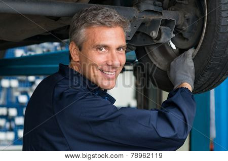 Portrait Of Happy Mature Mechanic At Repair Service Station Changing Tire