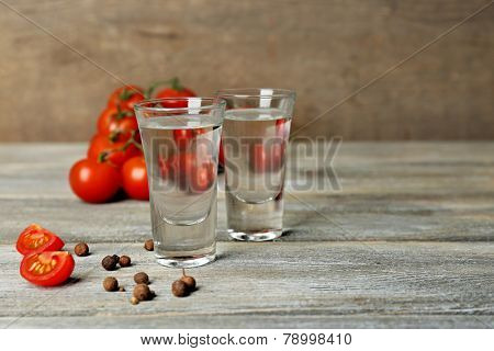 Glasses of ouzo and tomatoes on wooden table