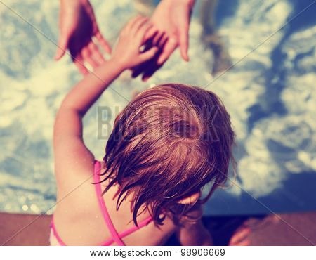 a small child reaching for her mother's hand in a local pool on a hot summer day toned with a retro vintage instagram filter effect app or action
