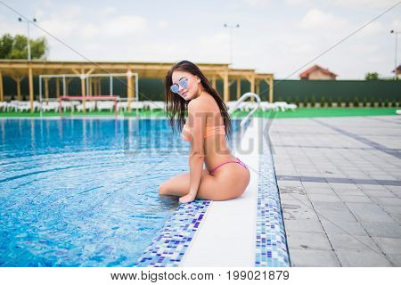 Sexy Young Woman Sitting On The Edge Of A Swimming Pool, Wearing Bikini While On Vacations In A Sunn