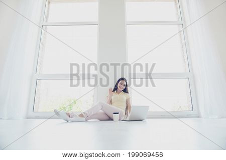 Hello There! Young Cheerful Brunette Lady Is Waving To The Camera While Having Video Call Sitting On