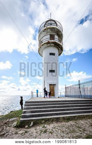 CABO TOURINAN SPAIN - MAY 17 2017: Tourists with RV motorhome camper at Cabo Tourinan - the most western point of Spain with lighthouse. Popular tourist and pilgrim destination. Beautiful old lighthouse on rocky cliff and Atlantic ocean in Spain.