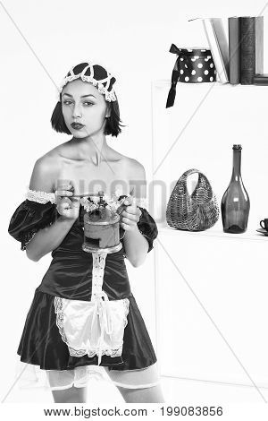 girl with pretty face in sexy servant costume and lace cap holding handle coffee grinder posing at kitchenware on shelves isolated black and white