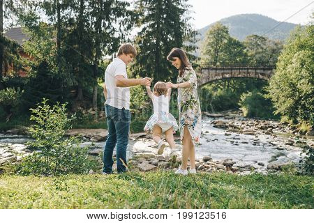 happy family play with daughter near the river in mountains, old bridge on backgeound