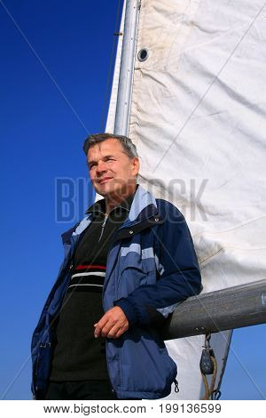 Successful held presentable handsome man against the background of the sail. He is 60 years old autumn. The sky is tall and blue. He looks into the distance. Today everything is good comfort calmness happiness. And tomorrow?