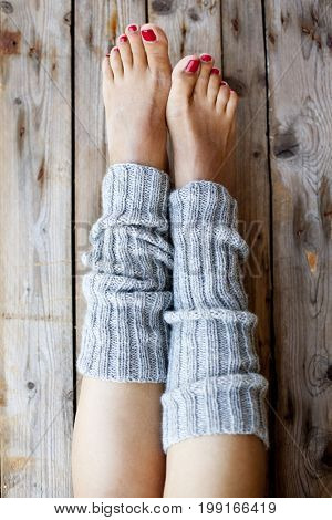 Woman's legs in knitted gray legwarmers closeup on wooden background.