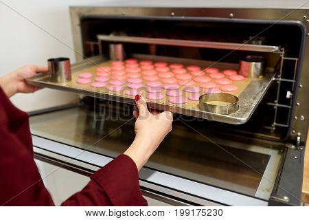 cooking, confectionery and people concept - chef with macarons on oven tray at bakery