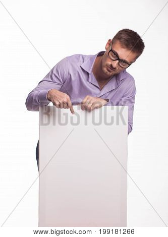 Young jocular man portrait of a confident businessman showing presentation, pointing paper placard gray background. Ideal for banners, registration forms, presentation, landings, presenting concept.