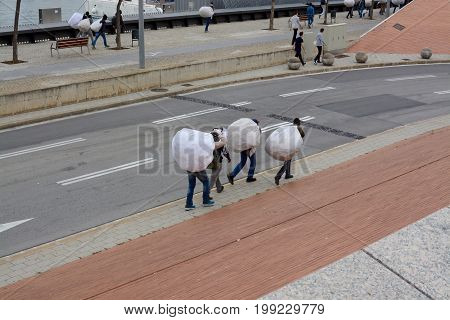 BARCELONA, SPAIN - MAY 02, 2017: Homeless male migrants walking down the road at Barcelona port with their possessions in white bags, Barcelona, Spain, Europe