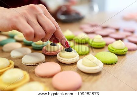 cooking, food and baking concept - chef decorating macarons shells at confectionery or pastry shop
