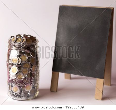 glass jar with full of mexican pesos coins and blackboard