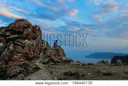 A man sitting on rocks in the evening on the cape of the island