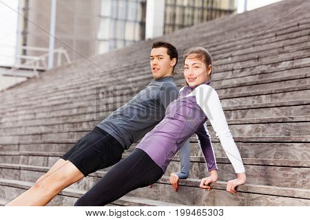Close-up portrait of sporty young couple holding reverse plank position, exercising together outdoors on city stairs