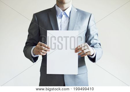 Photo of a man wearing light grey suit holding blank paper in his hands on white background