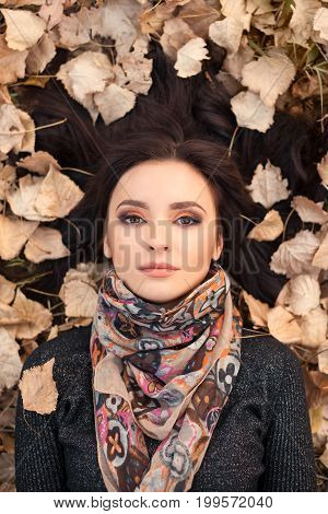 Autumn consept. Portrait of an autumn woman lying over leaves outside in fall forest. Beautiful mixed race Caucasian Asian young girl.